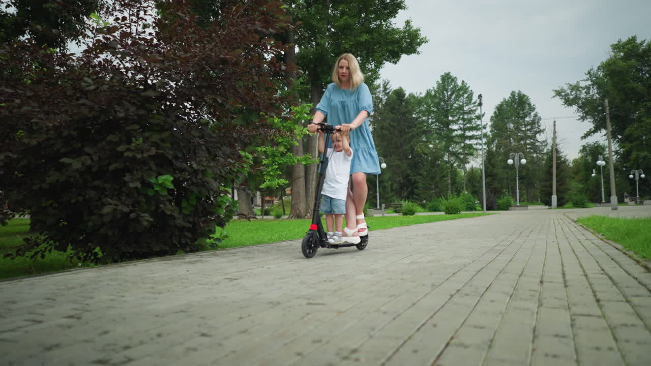 A mother and son riding a scooter down a smooth, interlocked walkway in a peaceful park