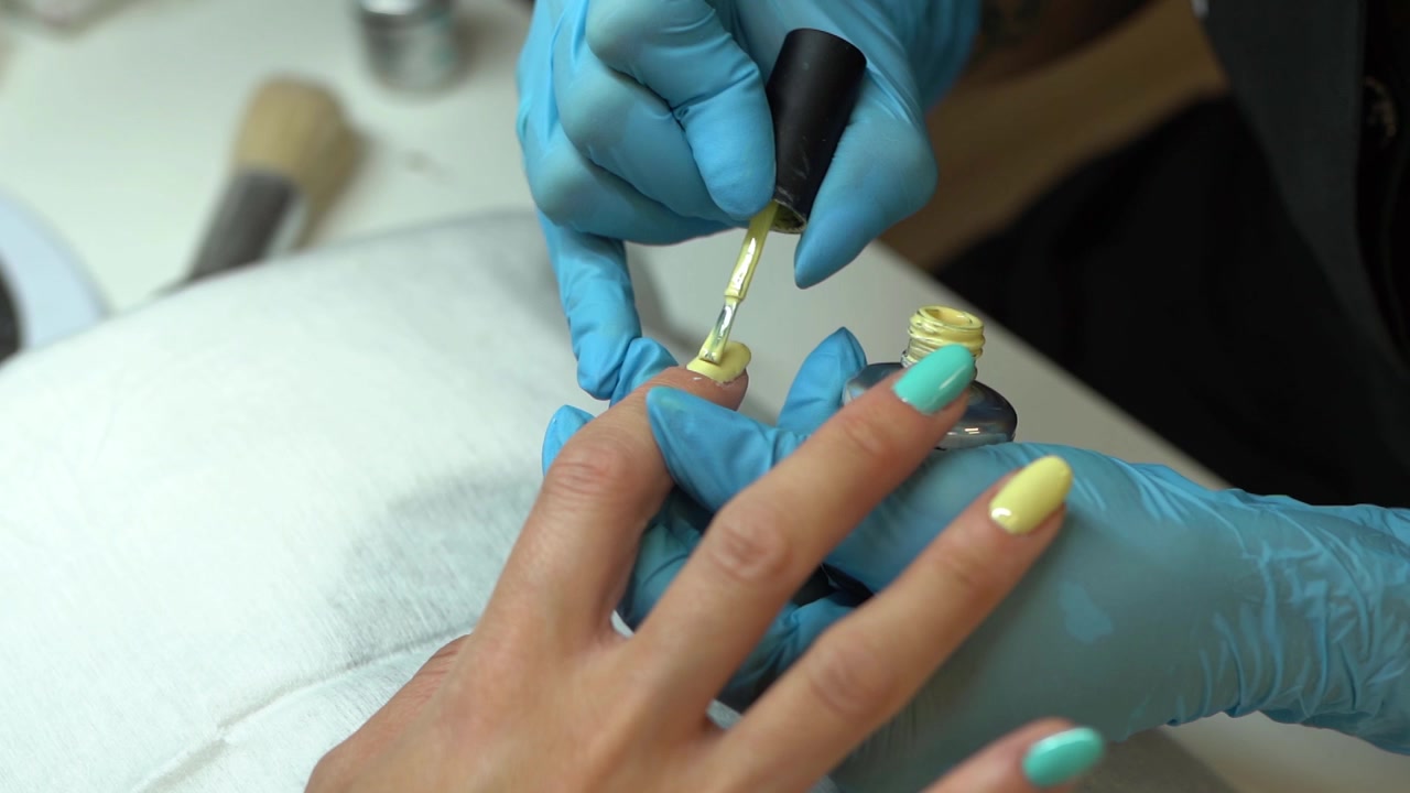 Closeup of beautician painting her clients nails in blue and yellow nail varnish