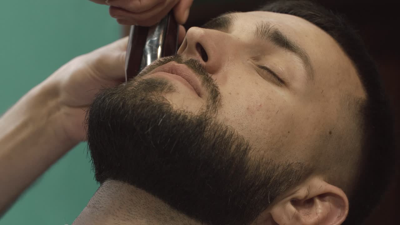 Mand får trimmet og plejet sit skæg hos en barber.