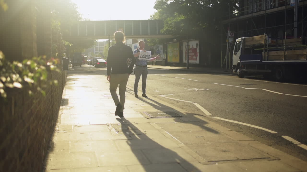 Guy holding a sign for hitchhiking and has thumb up, international sign for lifting, sunrise in London suburb