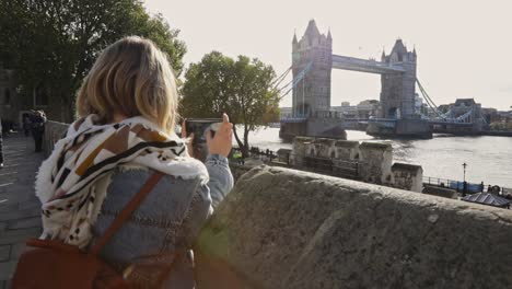 attractive blonde female traveler taking pictures of london tower bridge, back view