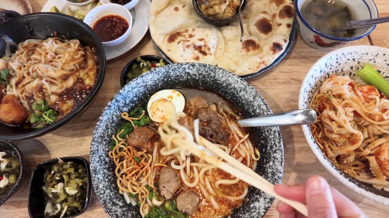 Pengambilan gambar dari atas: sumpit mengangkat mi dari mangkuk daging sapi pedas di Bangkok, Thailand.