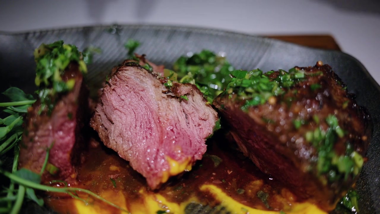 Primo piano di una bistecca alla griglia che viene affettata con un coltello e una forchetta in un ristorante.