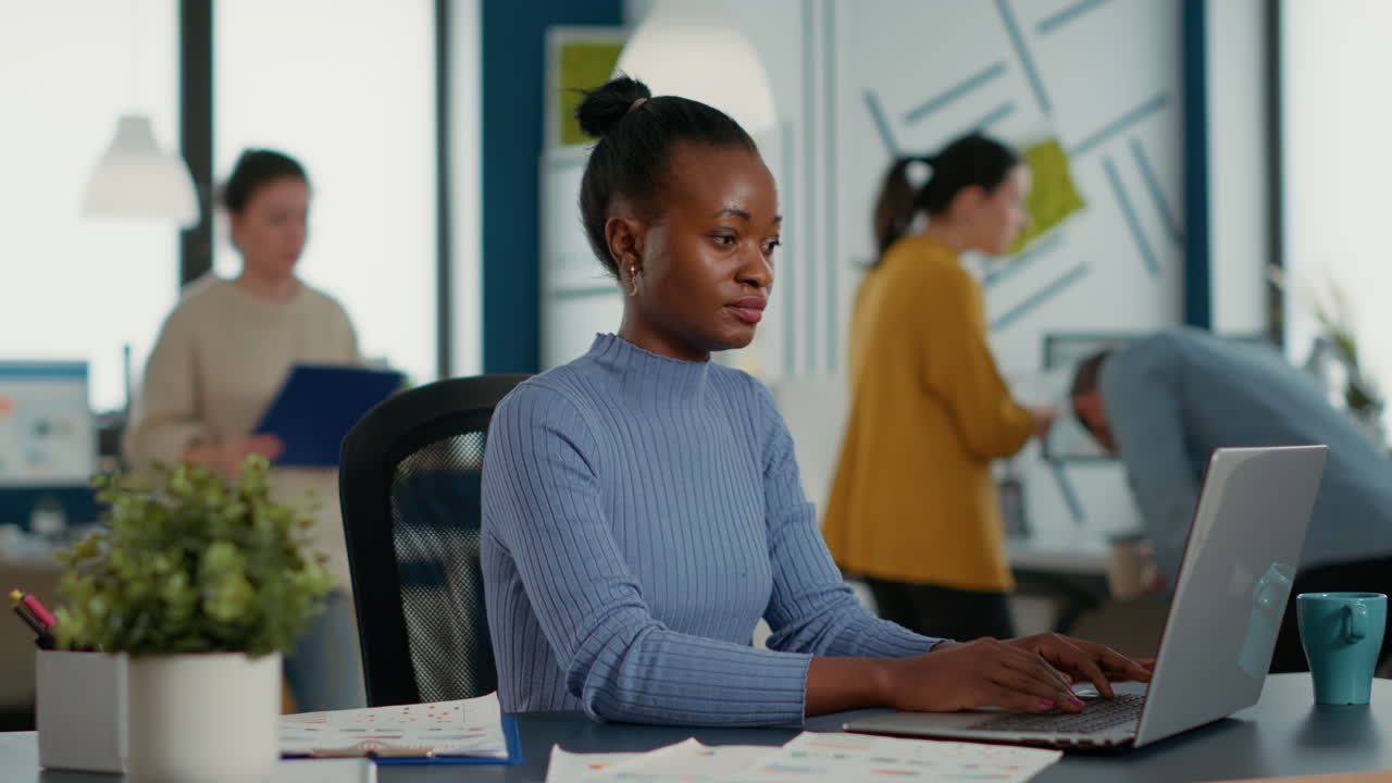 African american startup employee sitting at desk opening laptop and starting to type on keyboard