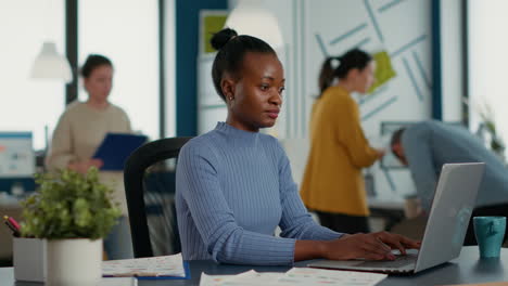 African-american-startup-employee-sitting-at-desk-opening-laptop-and-starting-to-type-on-keyboard