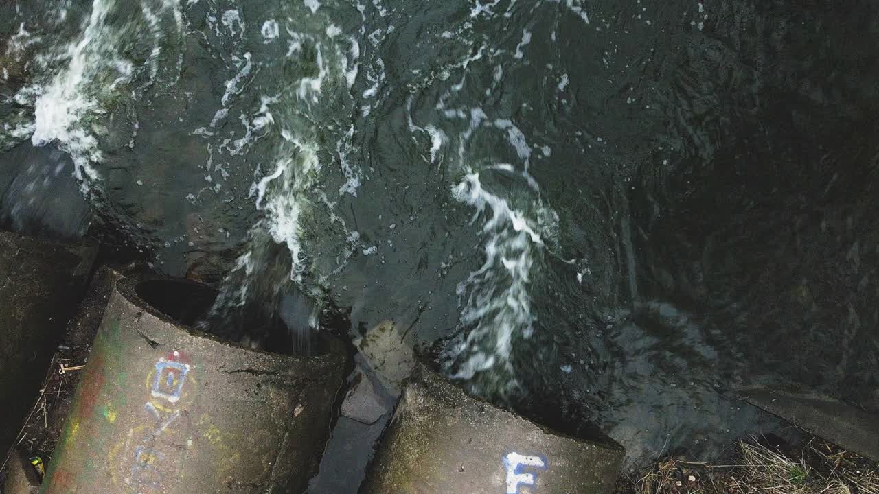 Terbang di atas selokan beton. Aliran air mengalir melalui pipa beton. Badan air yang tercemar di taman. Kamera ke bawah.