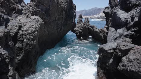 Rocky-ocean-inlet-at-Charco-del-Diablo,-Tenerife,-with-frothy-waves-crashing-between-jagged-cliffs