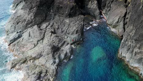 aerial view reveal of young male hiker standing on sharp, treacherous rocks by idyllic tropical cove