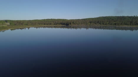 Aerial-shot-flying-over-a-blue-still-watered-lake-facing-a-beautiful-lush-green-forest-in-northern-Ontario-Canada