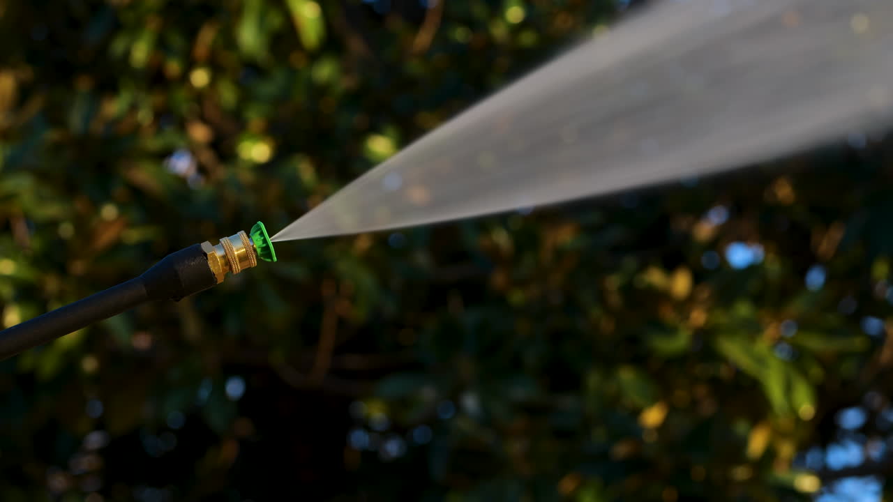 Power washer with green tip sprays high powered water jet with trees in background