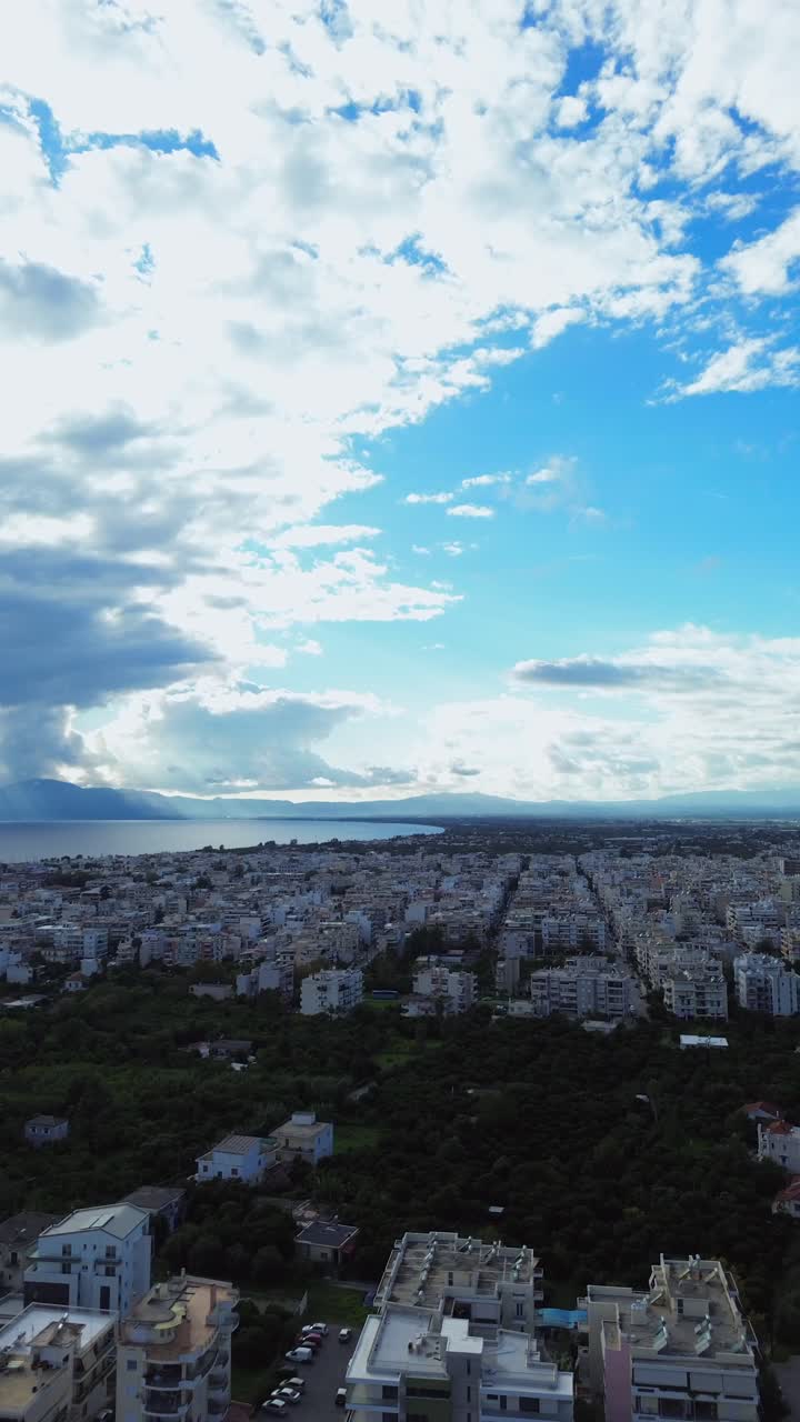Aerial bird's eye view, high angle vertical footage, cityscape of Kalamata city on a cloudy autumn day, Messinian gulf on background 4K
