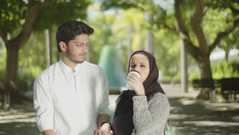 lovely muslim couple walking in park, drinking takeaway coffee.