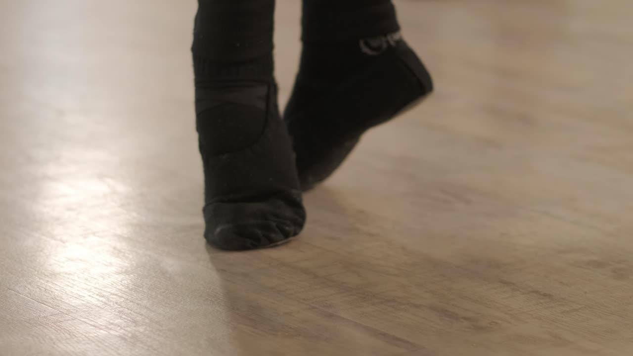 un grupo de jóvenes estudiantes de ballet con ropa de baile negra practicando posiciones en un amplio estudio de ballet con pisos de madera y barras montadas en la pared. expresiones enfocadas y movimientos sincronizados.