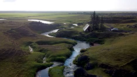 Travelers-cabin-in-Iceland's-countryside-next-to-a-river-flowing-by-mossy-rocks