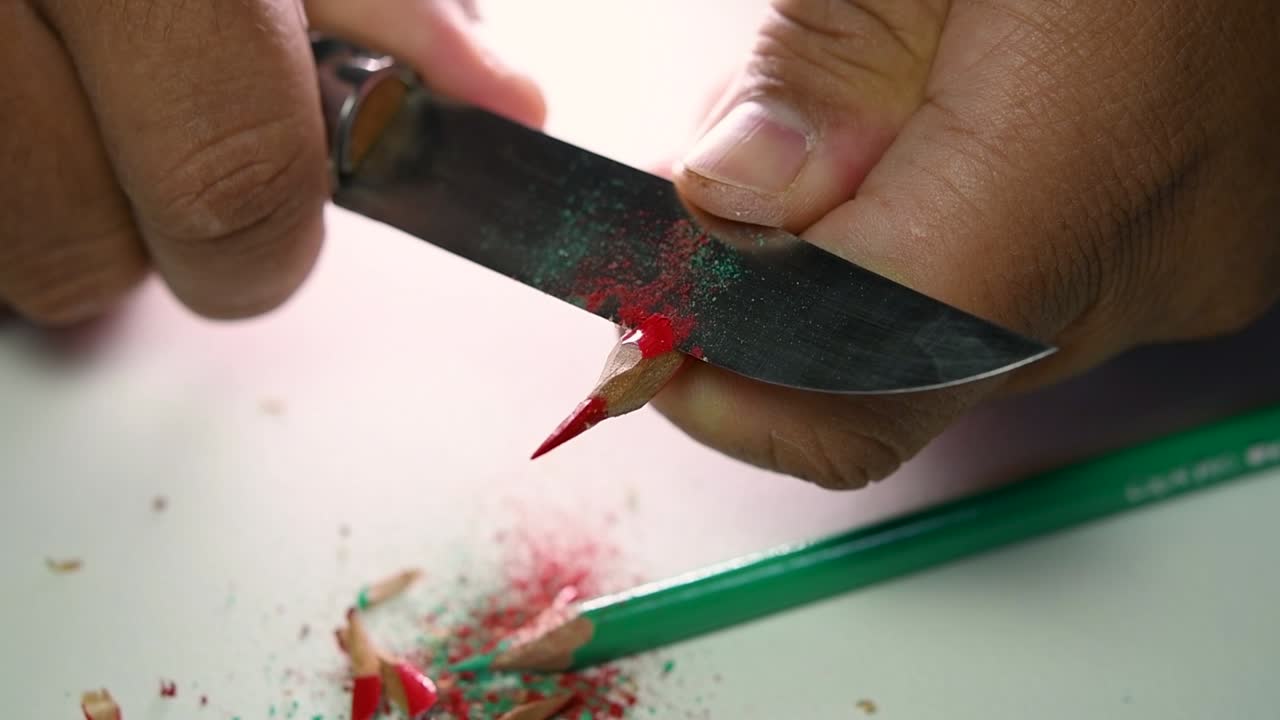 Filmato di mani che affilano lentamente una matita e alcune matite colorate con un coltello affilato.