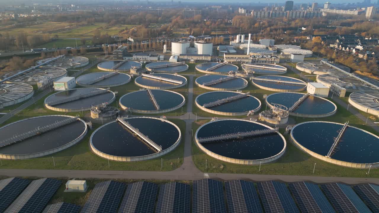 Detailed aerial view showing symmetrical circular clarifier basins filled with water at the Harnaschpolder wastewater treatment installation in the Netherlands during golden morning light