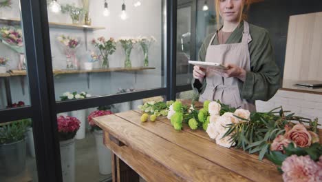 Asistente-De-Tienda-En-Floristería-Haciendo-Arreglos-Florales-Habla-Con-Su-Jefe-Mientras-Sostiene-Una-Tableta