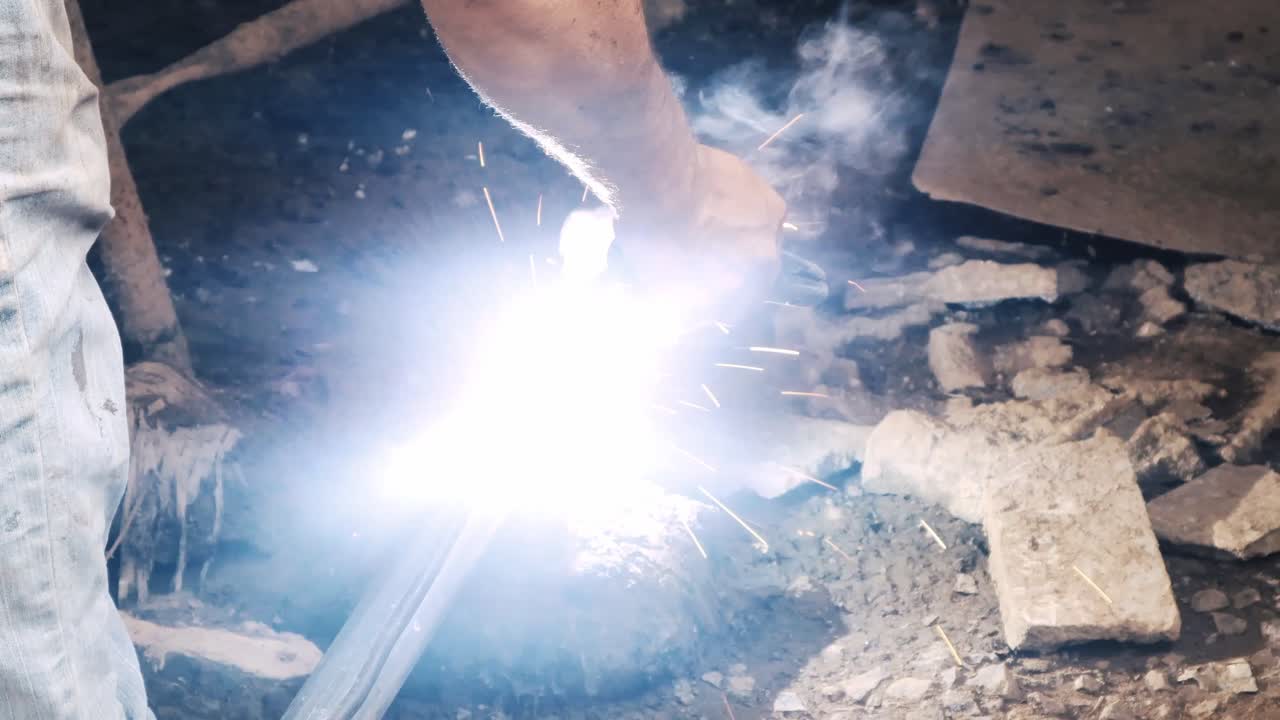 Professional welder employing industrial welding machine to put together two pieces of metal creating a metalic structure as part of his daily work at a local small business