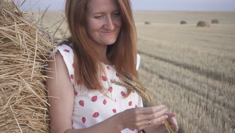 outdoor evening portrait of a beautiful young smiling girl near the round bale of hay in a wheat field