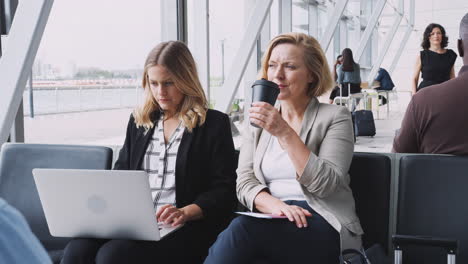 businesswomen sitting in airport departure working on laptop