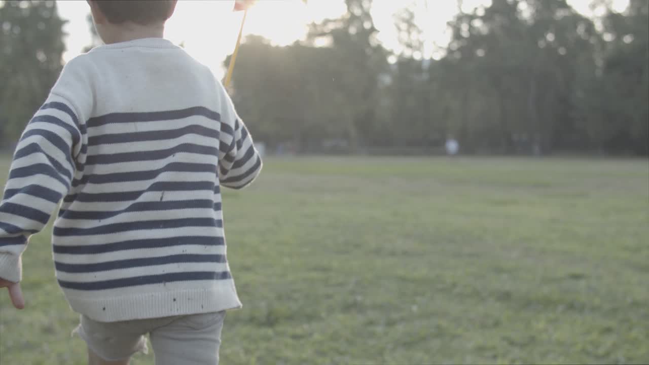 Back view of little boy running on lawn with paper fan