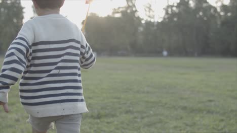 Vista-Trasera-Del-Niño-Corriendo-En-El-Césped-Con-Ventilador-De-Papel