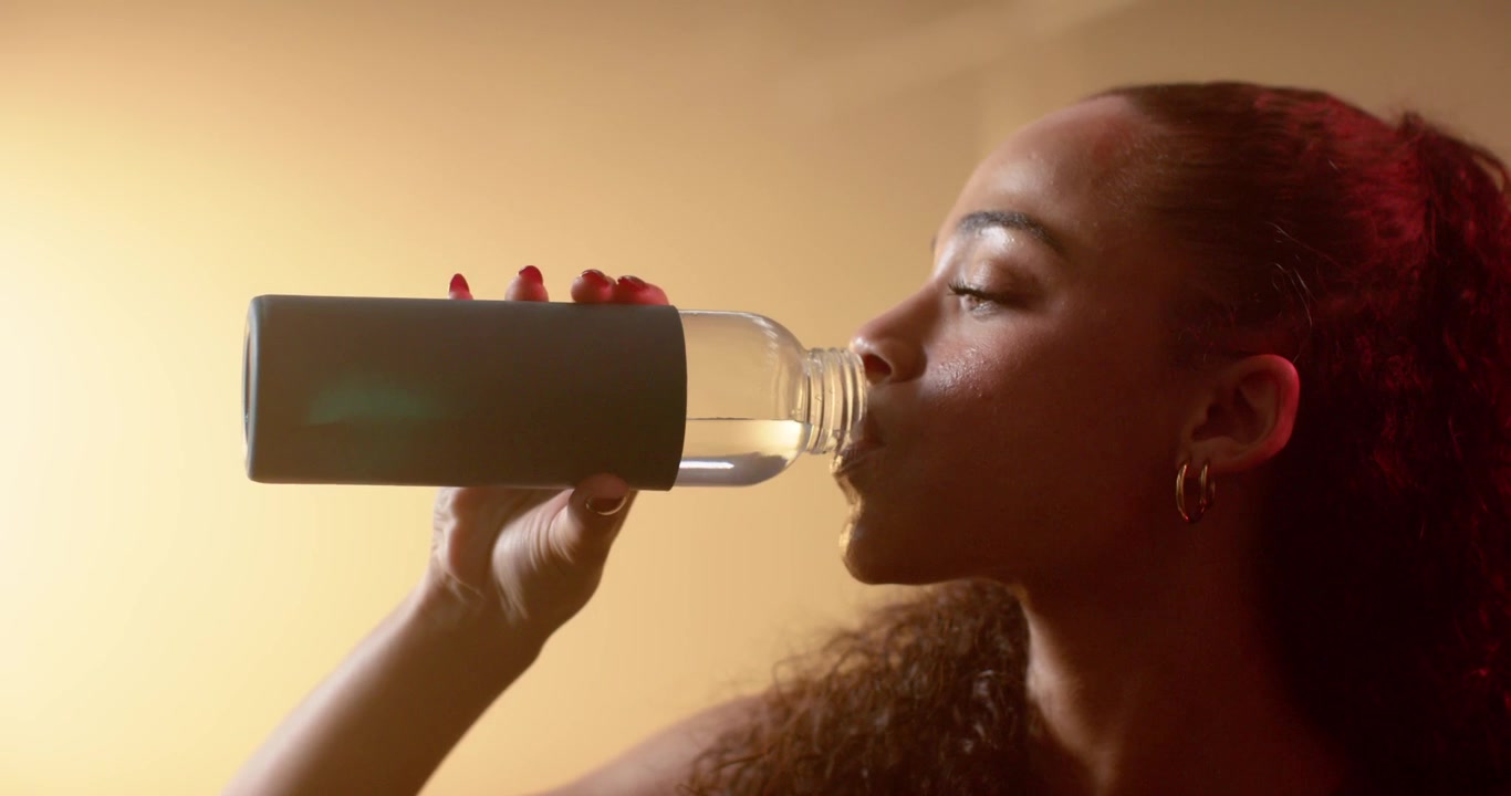 African American woman raising water bottle drinking inspecting reflecting at home, copy space
