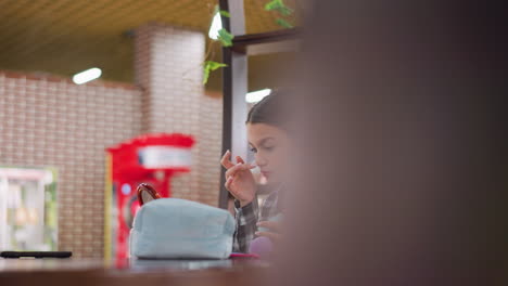 una joven frotando la mano en la nariz mientras se aplica maquillaje, artículos cosméticos esparcidos en la mesa con un espejo en el frente, el fondo borroso da atención al proceso de maquillaje y cuidado personal