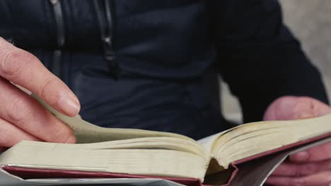 man sitting reading book, front close-up view of hand turning pages