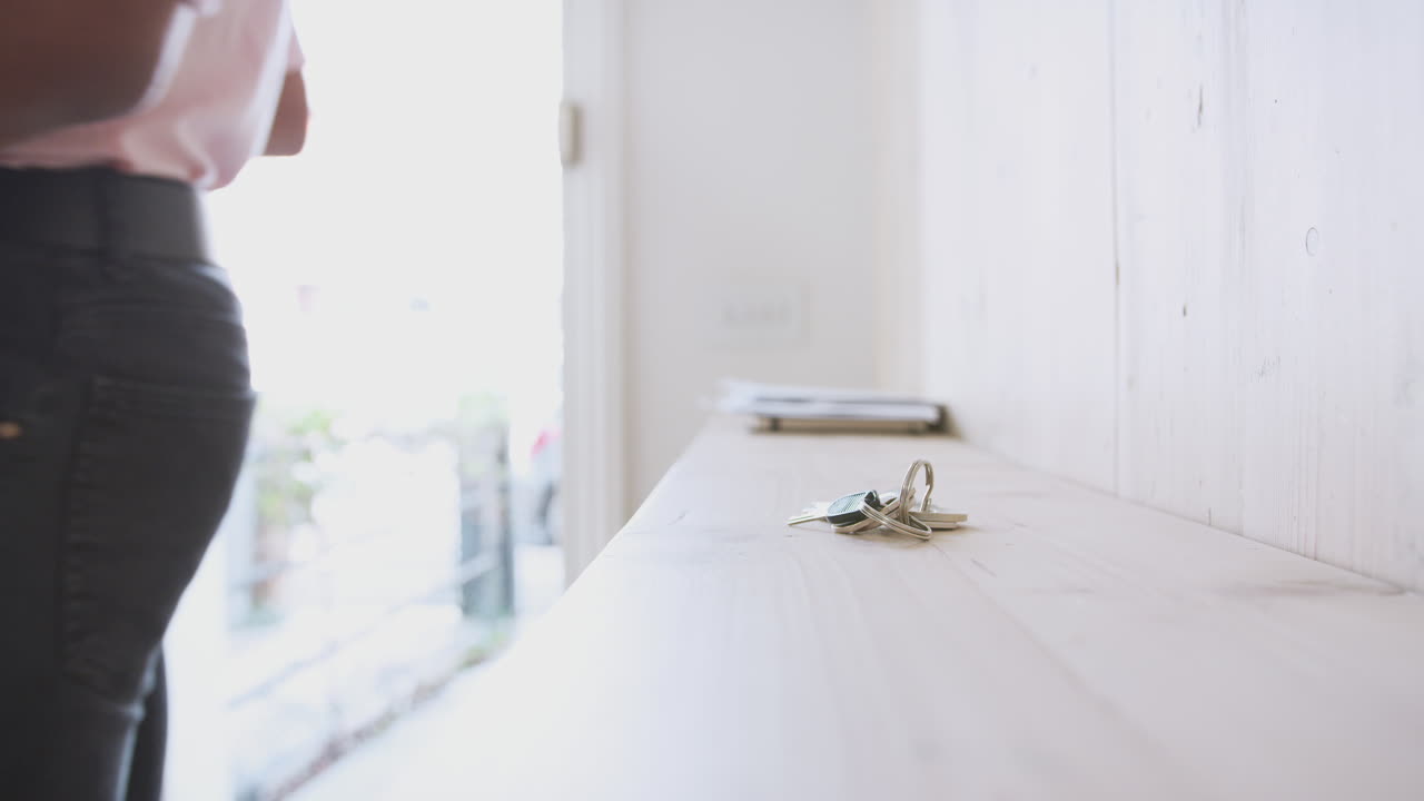 hombre que lleva a la hija bebé en la eslinga abre la puerta delantera de la casa y pone las llaves en el estante