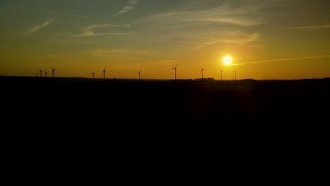 Fila-De-Turbinas-Eólicas-Girando-Siluetas-Oscuras-Contra-El-Cielo-Dorado-Del-Atardecer