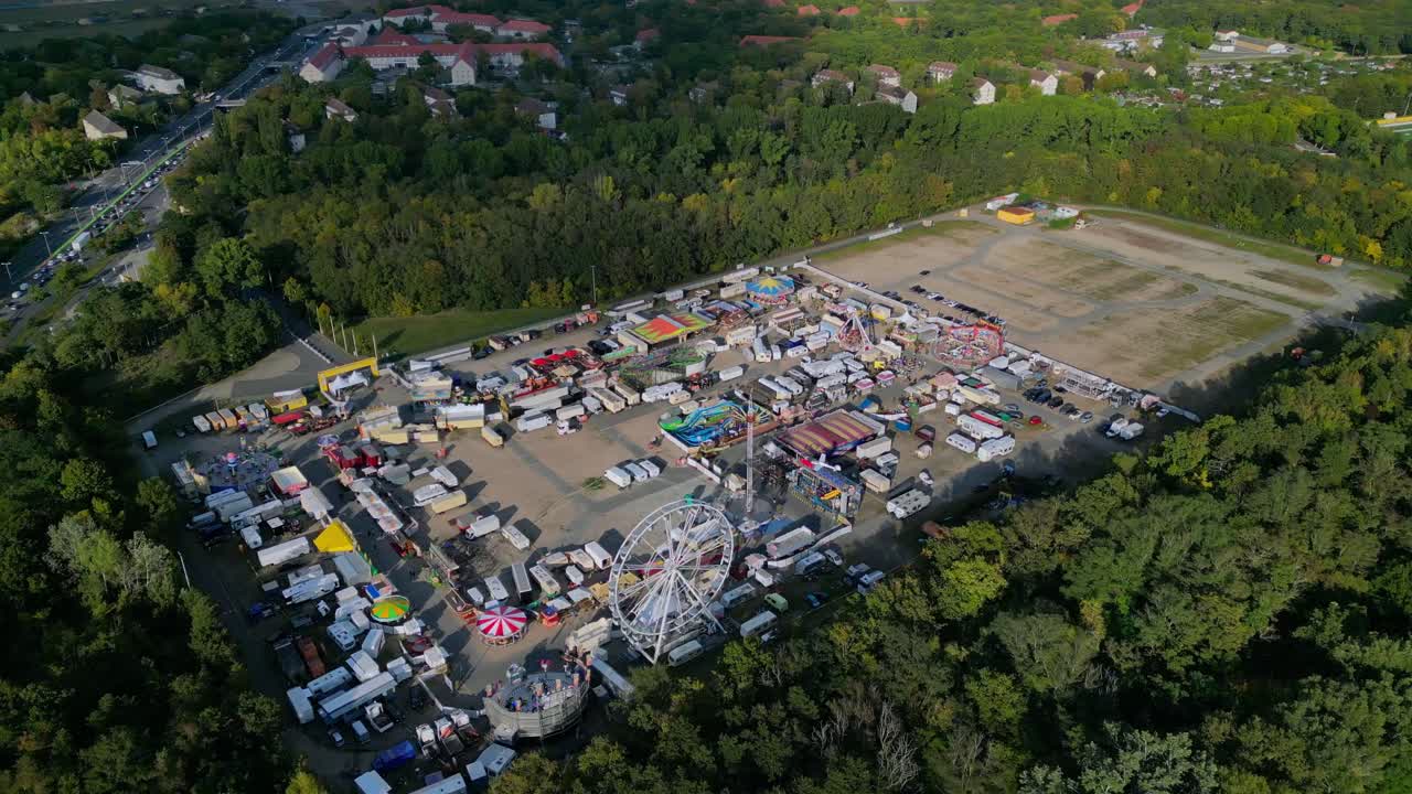 outdoor forest fairground, funfair, carnival with rides and stalls surrounded by forest. Dramatic aerial view flight circle drone footage