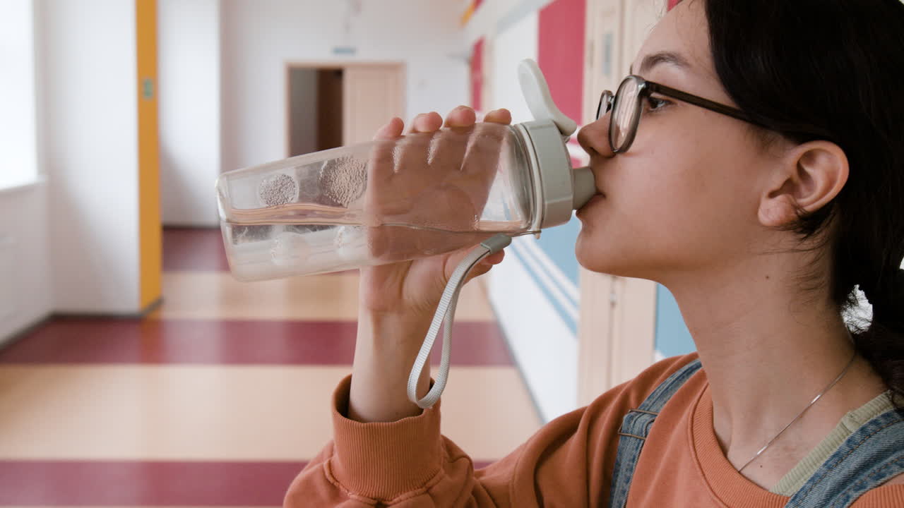 Student drinking water from a bottle in a school hallway