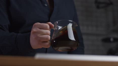 man shakes a glass pot with coffee inside