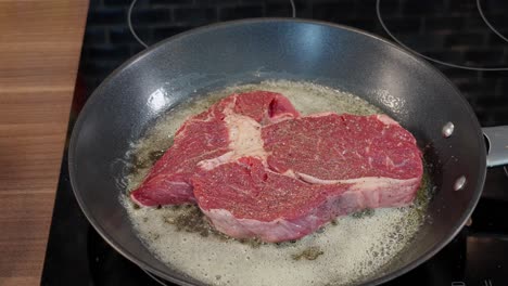 Hand-places-raw-entrecote-steak-in-pan-with-bubbling-butter,-ready-for-cooking,-60-fps