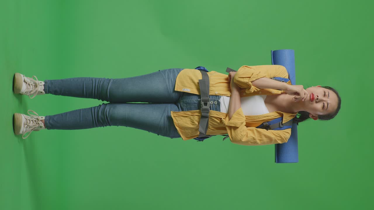 cuerpo lleno de excursionista femenina asiática con mochila de montañismo pensando en algo y mirando a su alrededor luego levantando su dedo índice mientras estaba de pie en el fondo de la pantalla verde en el estudio