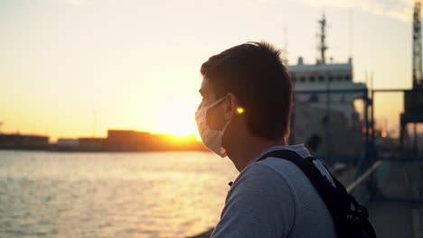 chico con mascarilla disfrutando de la vista del océano tranquilo durante la puesta de sol en el puerto de puerto ingeniero blanco, buenos aires, argentina