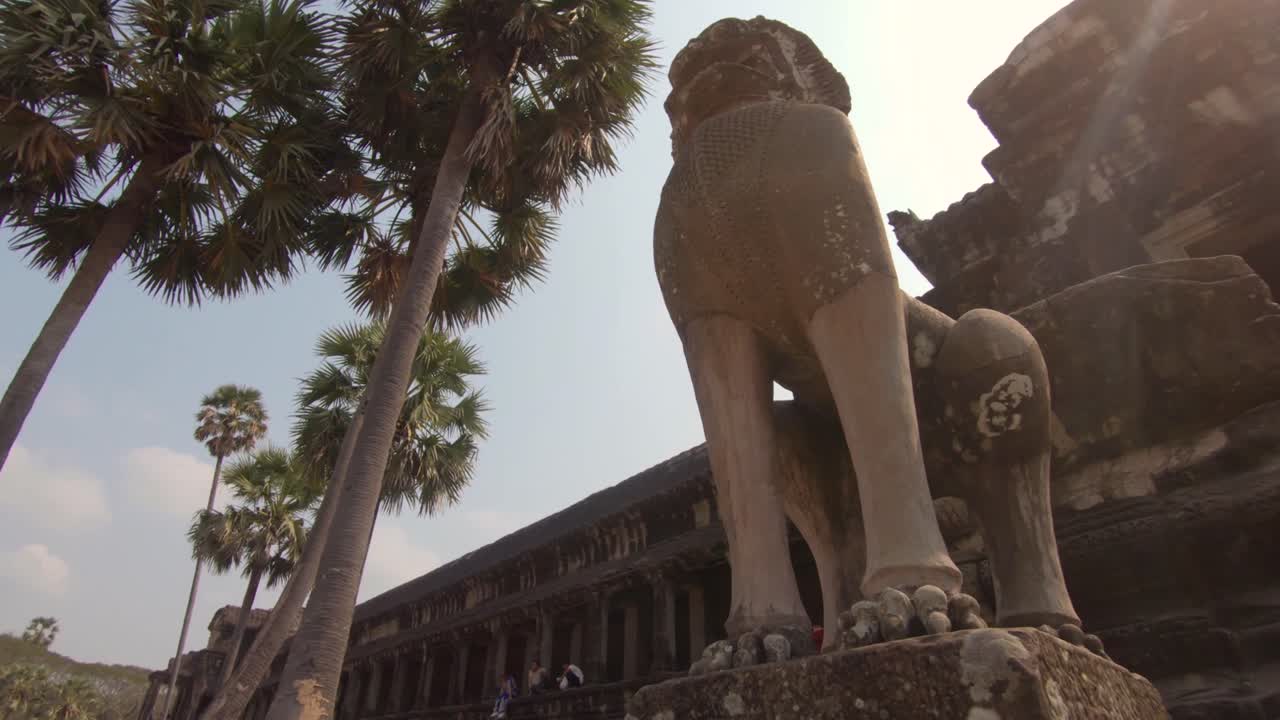 Walking past an animal statue under palm trees in Angkor Wat, Cambodia
