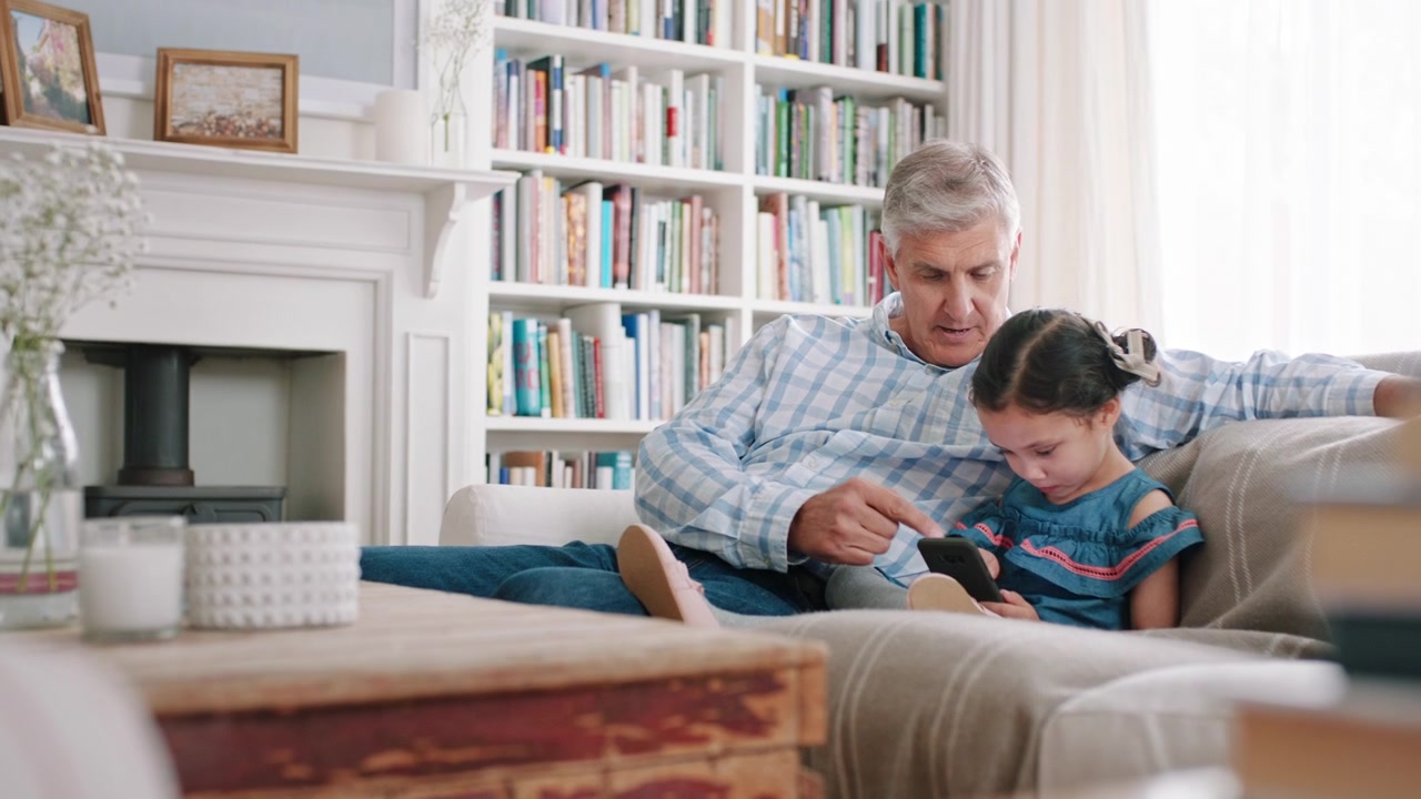 Grandfather and Granddaughter Using Smartphone Together on Sofa