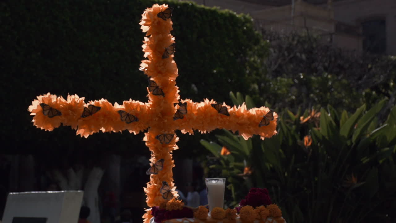 primer plano de un adorno de una cruz católica decorada con flores amarillas de cempasuchil y mariposas monarca durante la celebración del día de los muertos en méxico