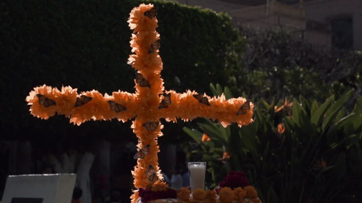 close-up of an ornament of a catholic cross decorated with yellow cempasuchil flowers and monarch butterflies during the celebration of the Day of the Dead in Mexico