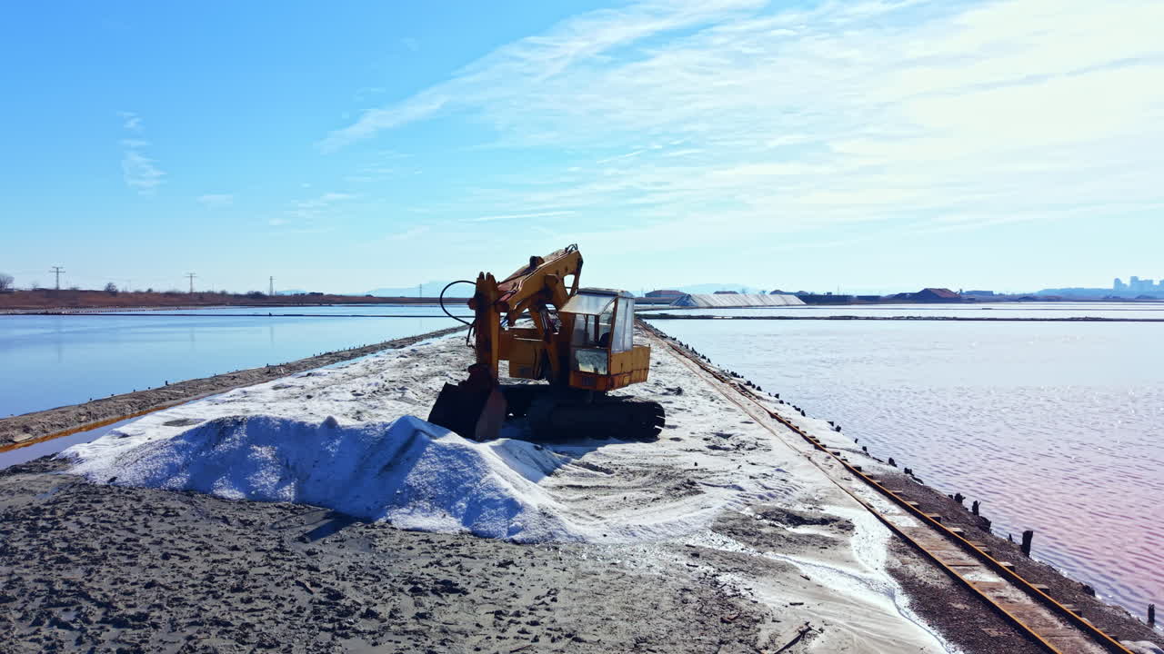 Un escavatore lavora per spostare il sale lungo la costa in una salina in una giornata di sole vicino a uno specchio d'acqua