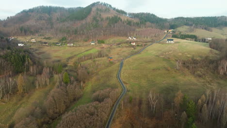 un camino sinuoso corta a través de colinas onduladas y bosques escasos, con un toque de vivienda rural en el fondo