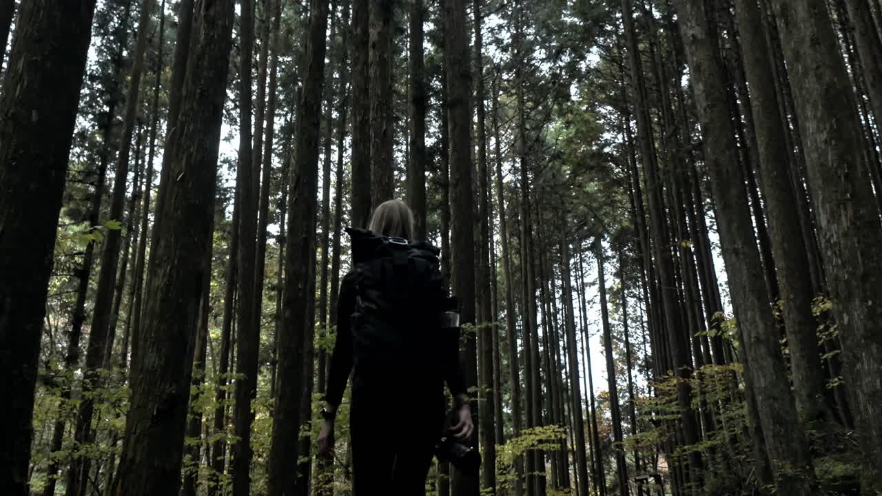 A cinematic video of a girl holding a camera in her hand as she walks with a backpack through the serene Nakasendo Forest in Japan.