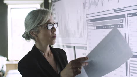 confident businesswoman checking papers with data on screen