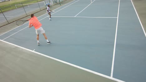 two diverse male friends playing doubles returning ball on outdoor tennis court in slow motion