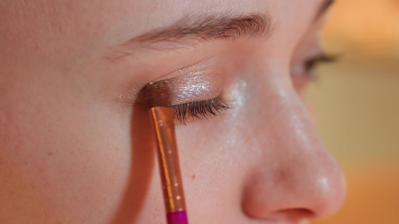 Primo piano di una giovane donna che applica un ombretto glitterato con un pennello da trucco