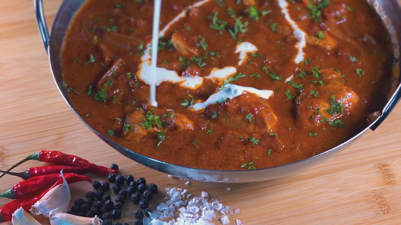 tiro giratorio de un curry malasio caliente en un plato balti mientras se vierte crema fresca encima