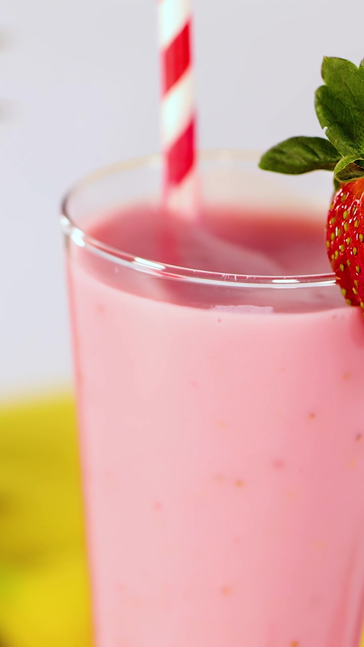 Frullato rosa di fragole in un bicchiere trasparente, guarnito con una fragola fresca, con luce intensa, in primo piano.