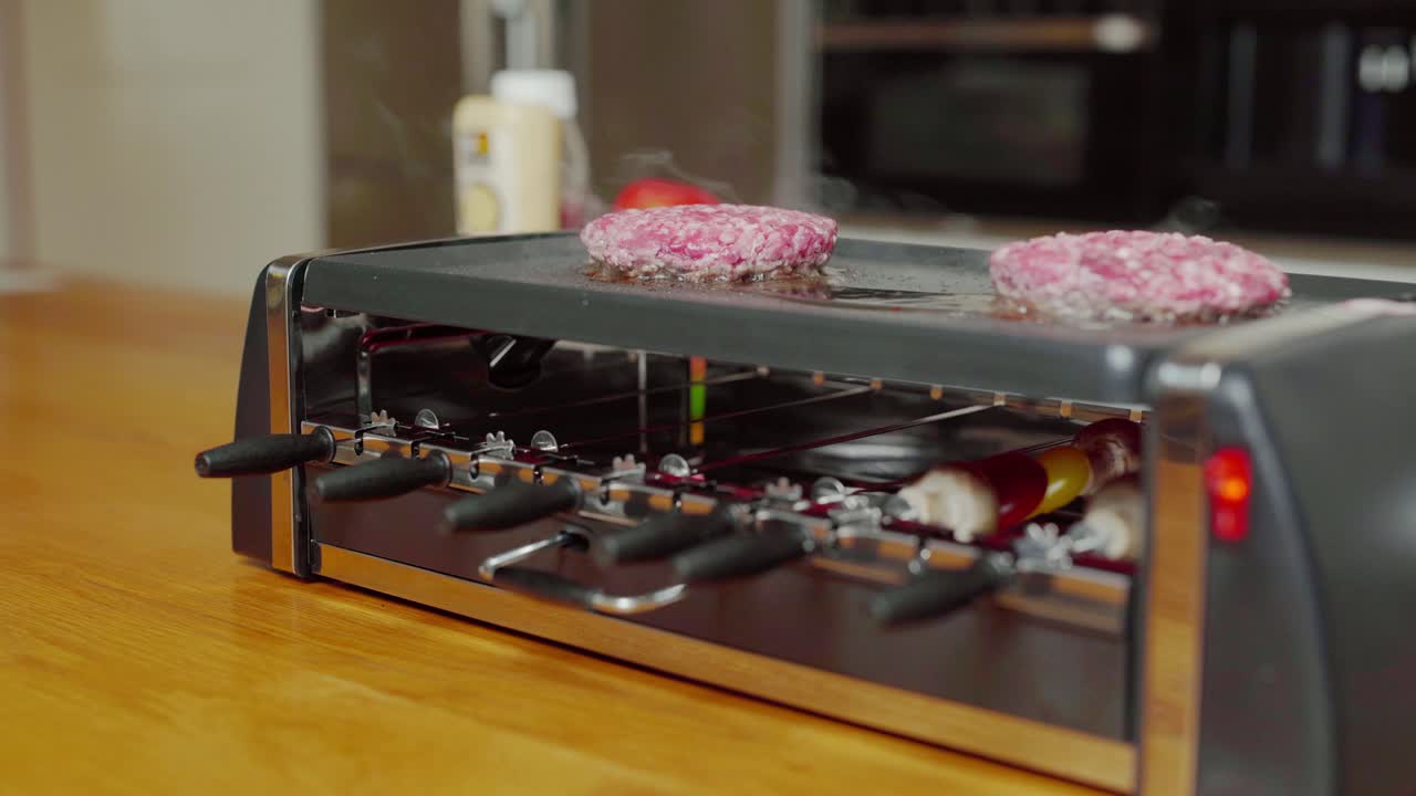 Versatile plancha grill, skewers rotating. Burgers grilling on top